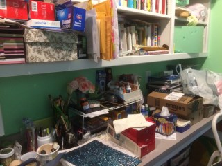 Workbench covered with art supplies, papers, fake flowers, boxes, and more.