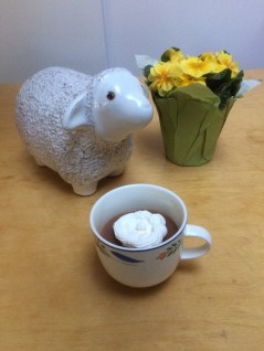 chocolate custard in a teacup with whipped cream and next to a ceramic sheep and flowers 