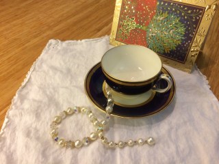 Tea cup on scalloped white napkin with necklace and Christmas card.