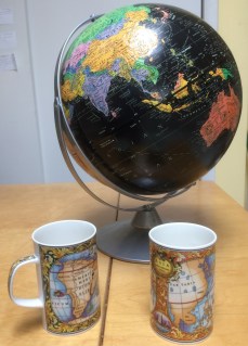 two mugs decorated with antique maps and an out-of-date globe